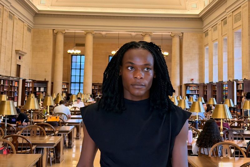 Deyner Caicedo Camacho walking through a vaulted library reading room lined with long tables and brass lamps